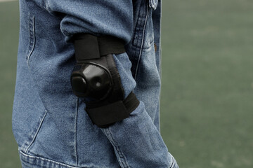 Close up of a black protective elbow pad worn over a blue denim jacket sleeve, side view for extreme sports safety, rollerskating, skateboarding, and active lifestyle concept