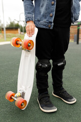 Cropped shot of a child holding a white penny board with orange wheels while standing on a dark grey rubberized playground surface, low angle view for extreme sports, childhood, and active lifestyle