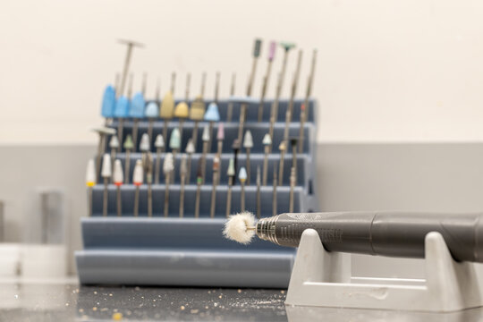 Dental laboratory drill handpiece with polishing brush attachment and assorted burs in rack, professional dentistry tools and oral care equipment concept