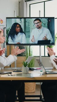 Medicine concept where attractive contented high-skilled diverse team of men and women-all are medics greeting with applauses their male main manager and african female workmate which hold video