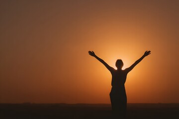 Fototapeta premium Silhouette of a person standing with raised arms facing the golden sunrise