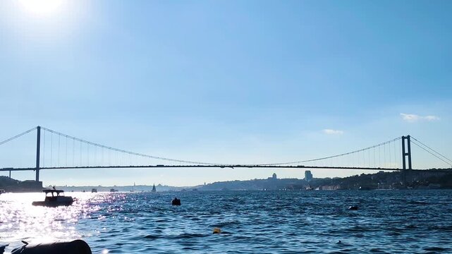 Iconic Bosphorus Bridge in Istanbul Under Bright Blue Sky with Sun Glare and Sparkling Water Reflection, Scenic View of the Strait Connecting Europe and Asia