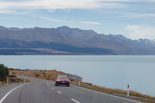 January 31, 2019, Lake Tekapo, New Zealand - Red Toyota Corolla driving on a winding road along Lake Tekapo with mountains in the background
