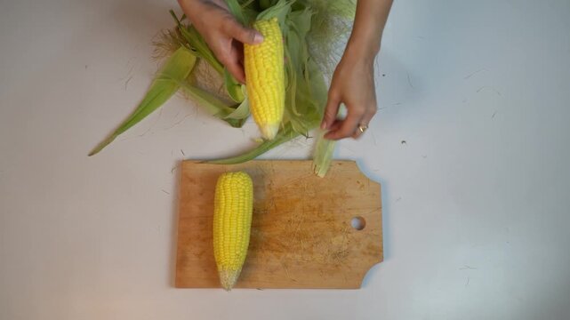 Top view of hands removing corn silk and husk from yellow maize
