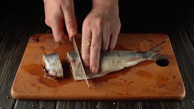 Hands skillfully slice through a fish on a wooden cutting board, demonstrating a clear progression of the cutting technique with Clupea parts and a rustic kitchen atmosphere