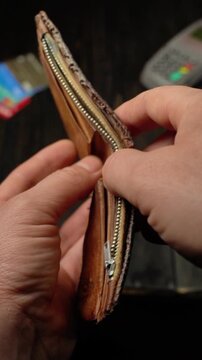 Hand holding a brown leather wallet with zipper, revealing its empty interior and card slots in a dimly lit setting with a wooden surface