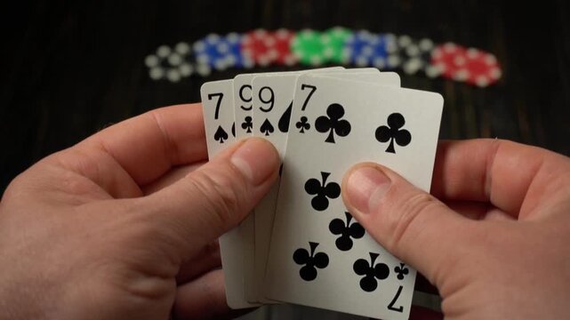 Hands hold a series of playing cards with two pairs, against the background of which are red, blue and green poker chips, creating a bright gaming atmosphere