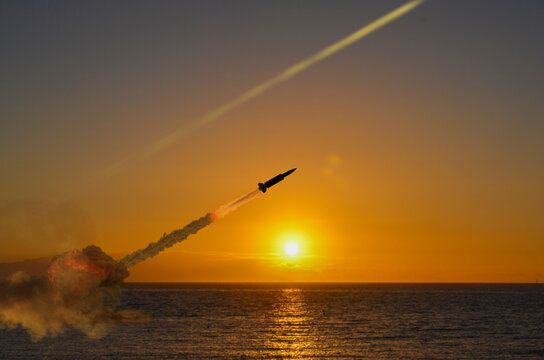 Military missile with smoke trail rises into sky at sunset over sea in conflict conditions