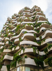 Striking contemporary architecture with organic, flowing lines of balconies adorned with abundant...