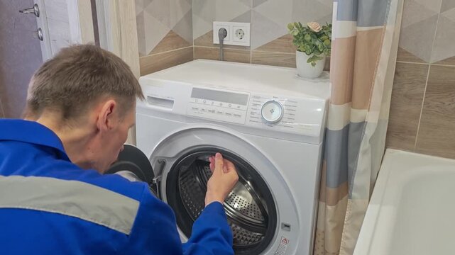 A technician fixes a washing machine in a small bathroom area.