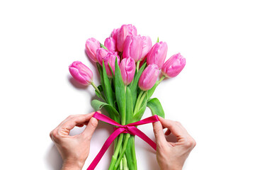 Woman hands tying pink ribbon on tulip bouquet