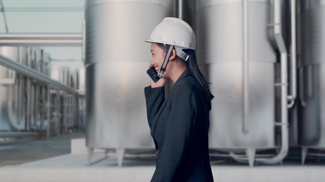 Side View of Asian Businesswoman Talking On Smartphone While Walking and Celebrating at Industrial Chemical Plant with Row of Stainless Steel Storage Silos