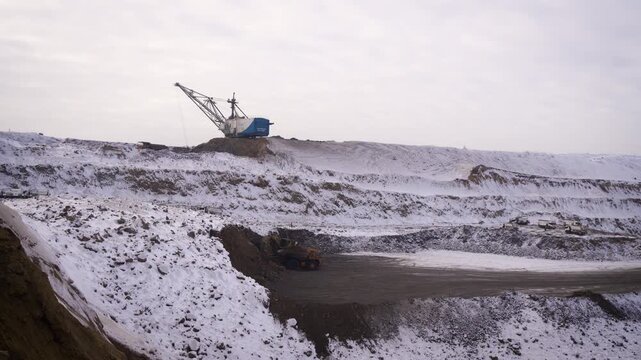 Wide Aerial View of Large Open Pit Coal Mine in Winter with Walking Dragline and Dump Trucks. Snowy Mining Quarry with Stepped Terraces.