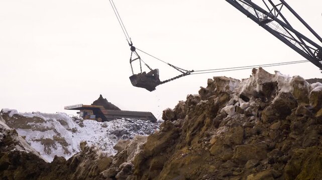 Walking Dragline Excavator Swinging Bucket Over Rock Face at Open Pit Mine in Winter. Heavy Mining Equipment at a Snowy Coal Quarry.