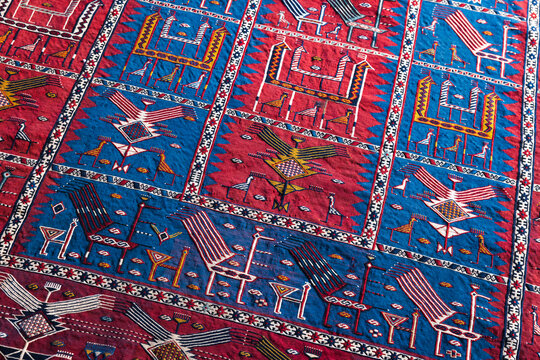 Richly patterned handwoven rug featuring bold red and blue panels, geometric motifs and embroidered tribal designs. Decorative textile conveys tradition, craftsmanship and warm bohemian interior style