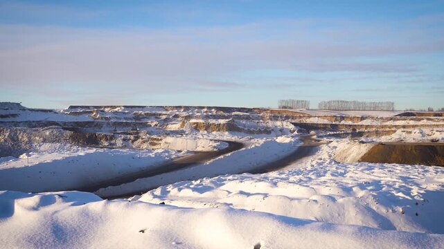 Panoramic Winter View of Large Open Pit Coal Mine with Dragline Excavator on Rim. Snowy Quarry with Winding Haul Road and Blue Sky.