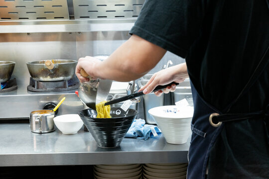 A rich tonkotsu ramen is served on a wooden counter under warm lighting, featuring a creamy pork bone broth with a glossy surface. The noodles are fully immersed, absorbing deep umami flavors. Topping
