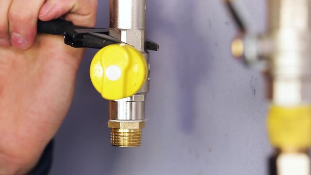 Close-Up of Yellow Gas Ball Valve with Brass Fitting on a Gas Pipe. Plumber Hand Inspecting Gas Shutoff Valve During Installation.