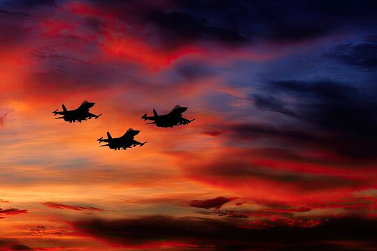 Silhouette of three fighter jets soaring through a vibrantly colored sunset sky