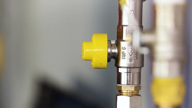 Close-Up of Hand Turning Yellow Gas Ball Valve on Chrome Gas Pipe with MOP Marking. Gas Technician Operating Shutoff Valve During Maintenance.