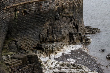 Fototapeta premium Historic stone seawall with rocky shoreline and pebbled beach
