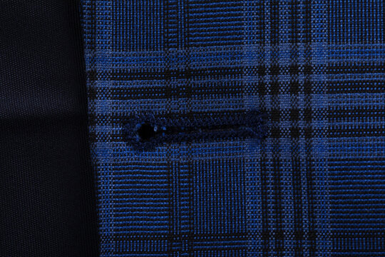 Close-up of blue plaid patterned fabric with a buttonhole, showcasing textile texture and detailed weaving.