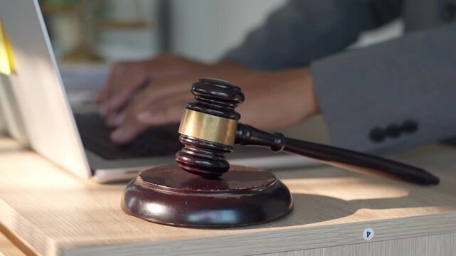 Judge gavel on desk with lawyer working on laptop in modern office, representing legal system, justice, law firm, and digital legal technology. Professional business and legal concept.