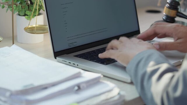 Hands type on laptop near stacks of papers. Document holder moves beside keyboard. Desk holds plants and legal symbols