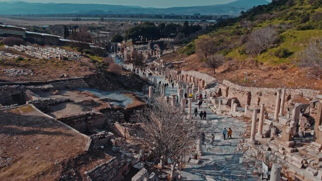 Elevated view of the ancient marble road in Ephesus, Izmir, Turkey. Ruins, columns, stone structures, hills and visitors create a scenic archaeological landscape rich in history and heritage.