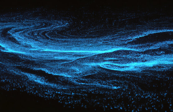 Electric blue bioluminescent plankton illuminate crashing waves in a dark night sea. The glowing light creates sparkling, swirling patterns, capturing a rare and magical natural phenomenon