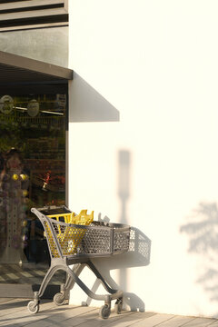 Shopping cart with soft shadow on clean wall, minimalist retail scene, modern sunlight aesthetic composition.