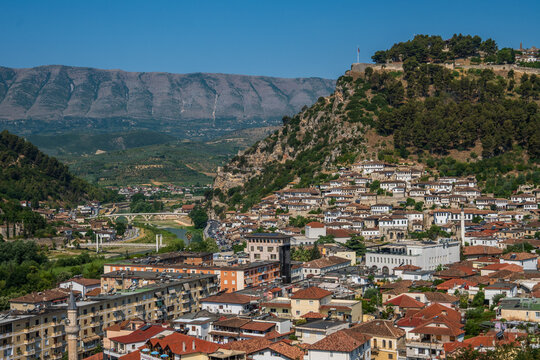 An expansive daytime panorama captures Berat city, the Osum River valley, and a historic castle crowning the hill in Berat, Albania.