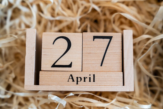 Wooden calendar with the date 27 and the month April displayed on a light straw background. Suitable for time management, planning, or seasonal themes.