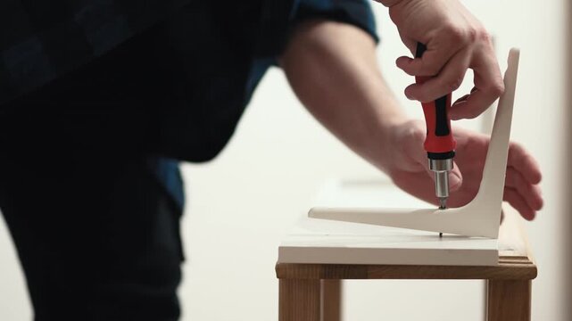 Close up of man screwing bolt into wall shelf with manual screwdriver, DIY home repair, 4K.