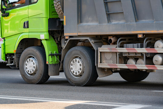 Green Dump Truck With Dual Rear Wheels Driving on Road Close-Up of Trailer and Tires