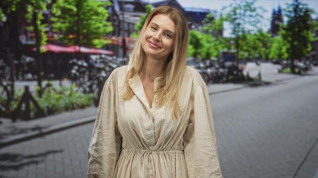 Blonde woman smiles with a slight head tilt and relaxed posture, beige linen dress cinched at waist, small pendant necklace, tree lined street scene; contentment.