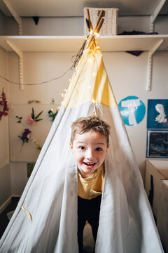 Portrait of cute boy peeking out from play tent in classroom