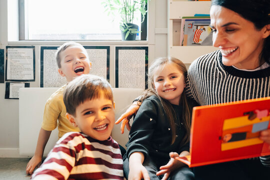 Cheerful kindergarten students spending leisure time with female teacher at preschool