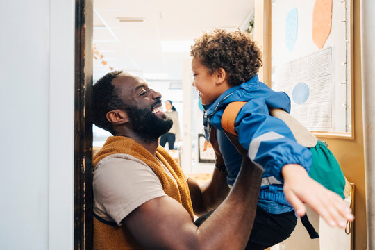 Side view of happy teacher holding boy in arms while standing at classroom doorway
