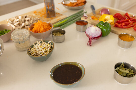 Small green ceramic bowl is sitting on countertop among bell peppers, carrot, grater, spices