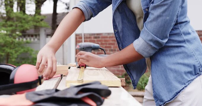 African American woman placing plank, clamping and measuring tape at yard workbench for sawing