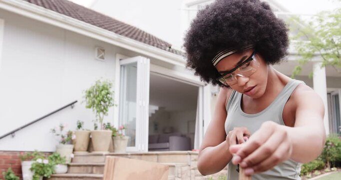 Aligning tool, African-American woman in goggles, headband using sander and smoothing edge on patio