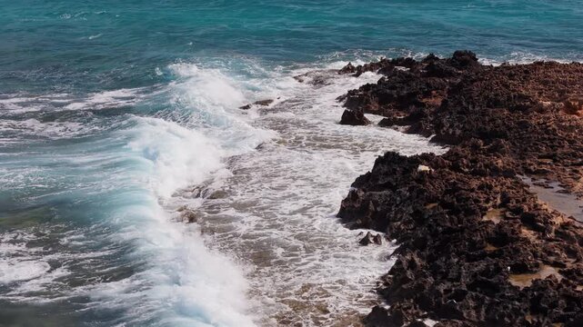 Aerial slow motion drone view of waves crashing against rugged dark rocks in Cyprus