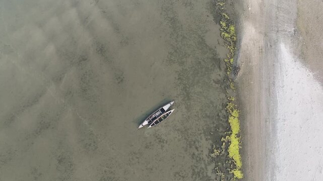 Aerial top down view of two traditional wooden boats floating gently on calm, shallow water near a mossy shoreline, evoking tranquility and peacefulness