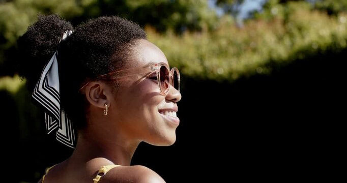 Adult African woman in yard facing sun turning to lens smiling adjusting sunglasses, copy space