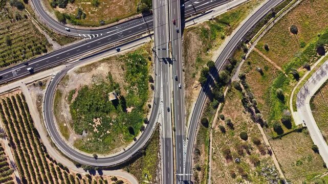 Vehicles travel on intersecting roads in a rural area, with green fields and patches of land visible nearby. The layout shows curves and straight paths in the landscape.
