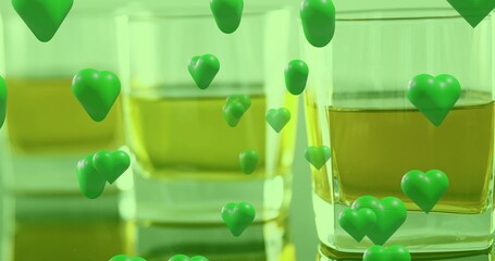 Obraz premium Showing two clear square tumblers filled with amber liquid on glossy counter, green hearts hovering