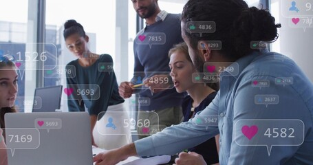 Meeting team wearing shirts leaning over laptop, discussing metrics with floating icons in office © vectorfusionart