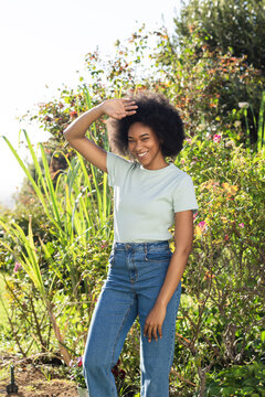 Woman standing in garden shading eyes from sunlight, smiling, wearing tee and high-waisted jeans