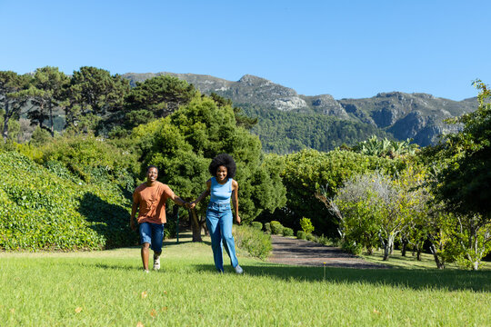 Man and woman are walking hand-in-hand across grassy lawn, starting from path and exploring garden